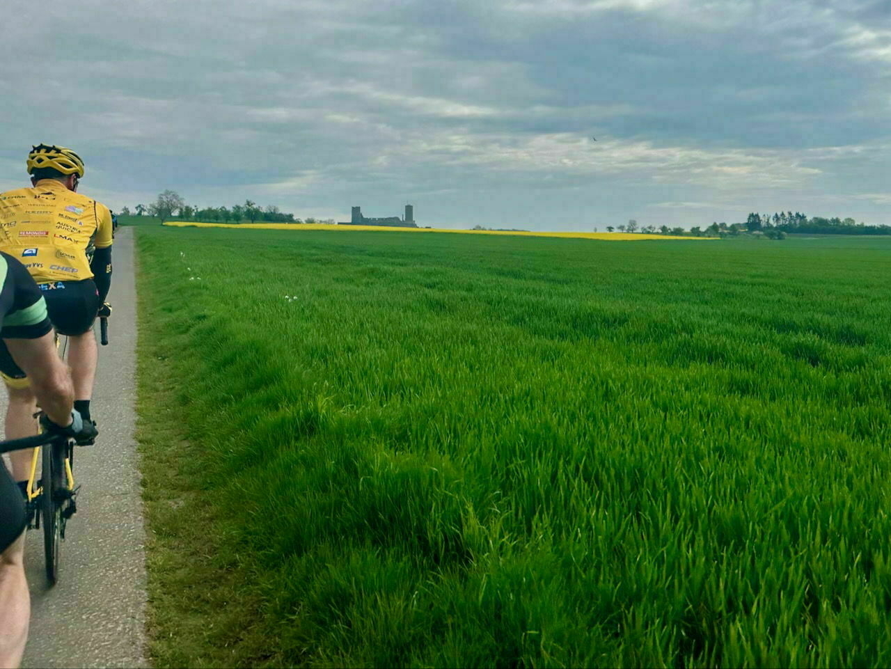 A field, on the Horizon a Rapps field and a castle. In front, only in sections two racing cyclists.