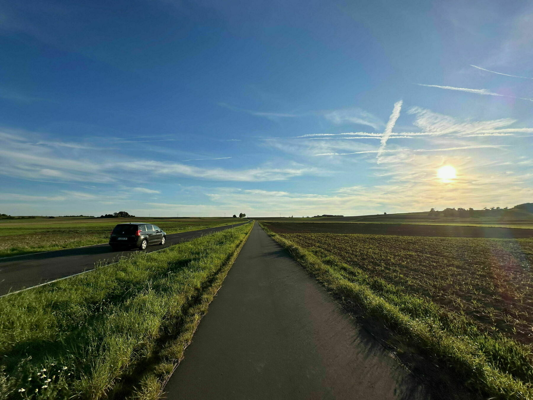 Road with car driving towards sunset with bike lane next to it.